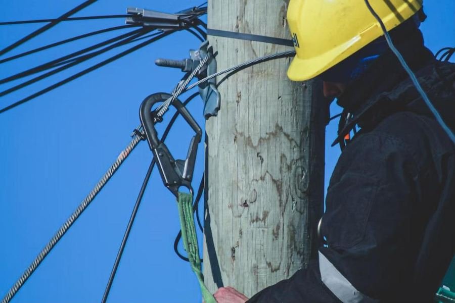 Lineman in a yellow hard hat working on an aerial cable pole