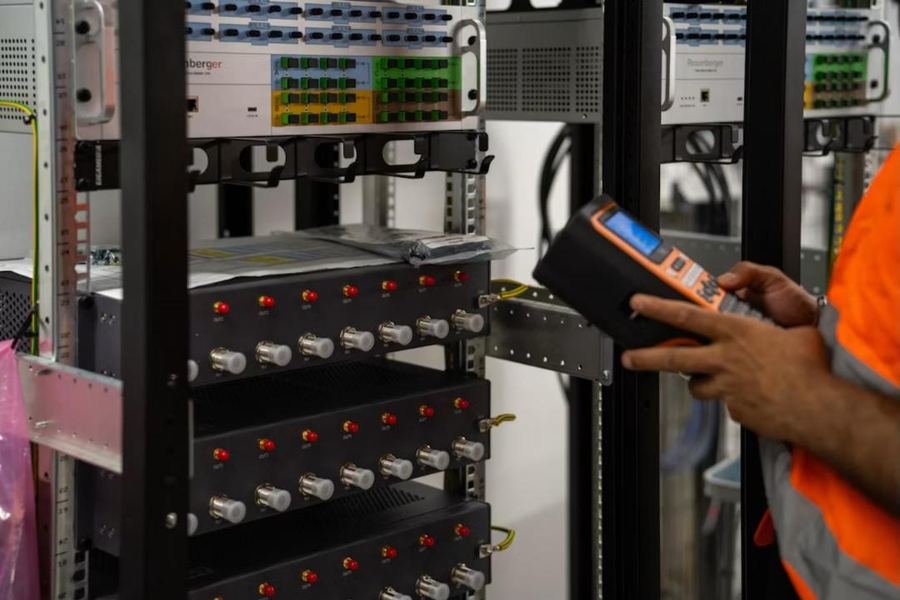Technician checking a telecom rack with a handheld test meter